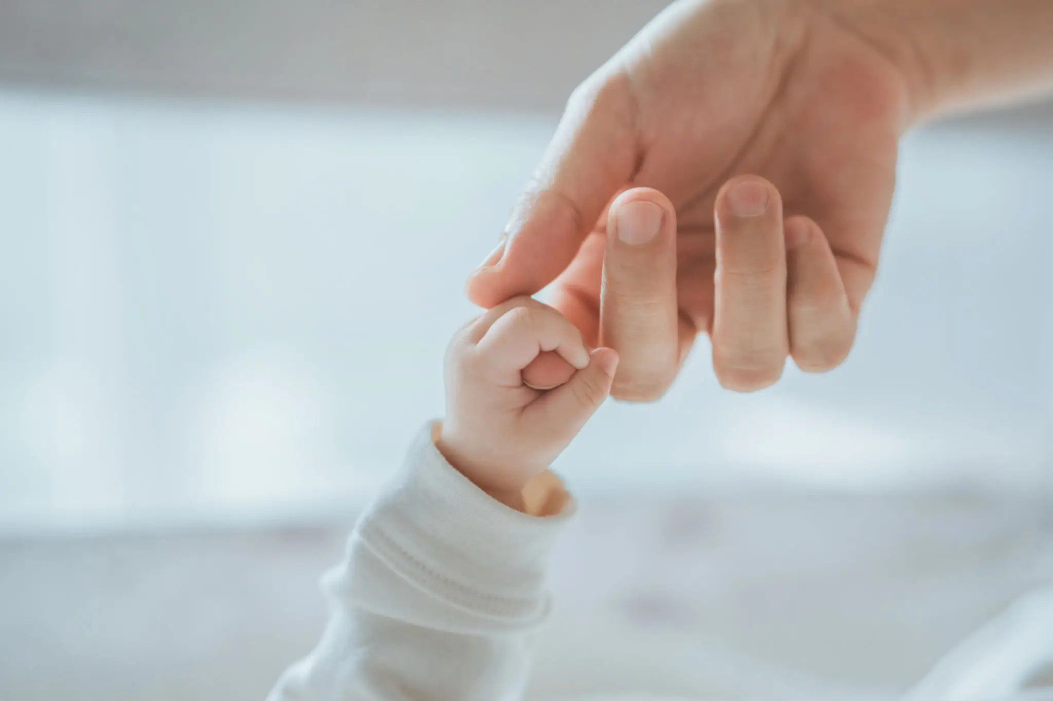 Adult hand gently holding a baby's hand.