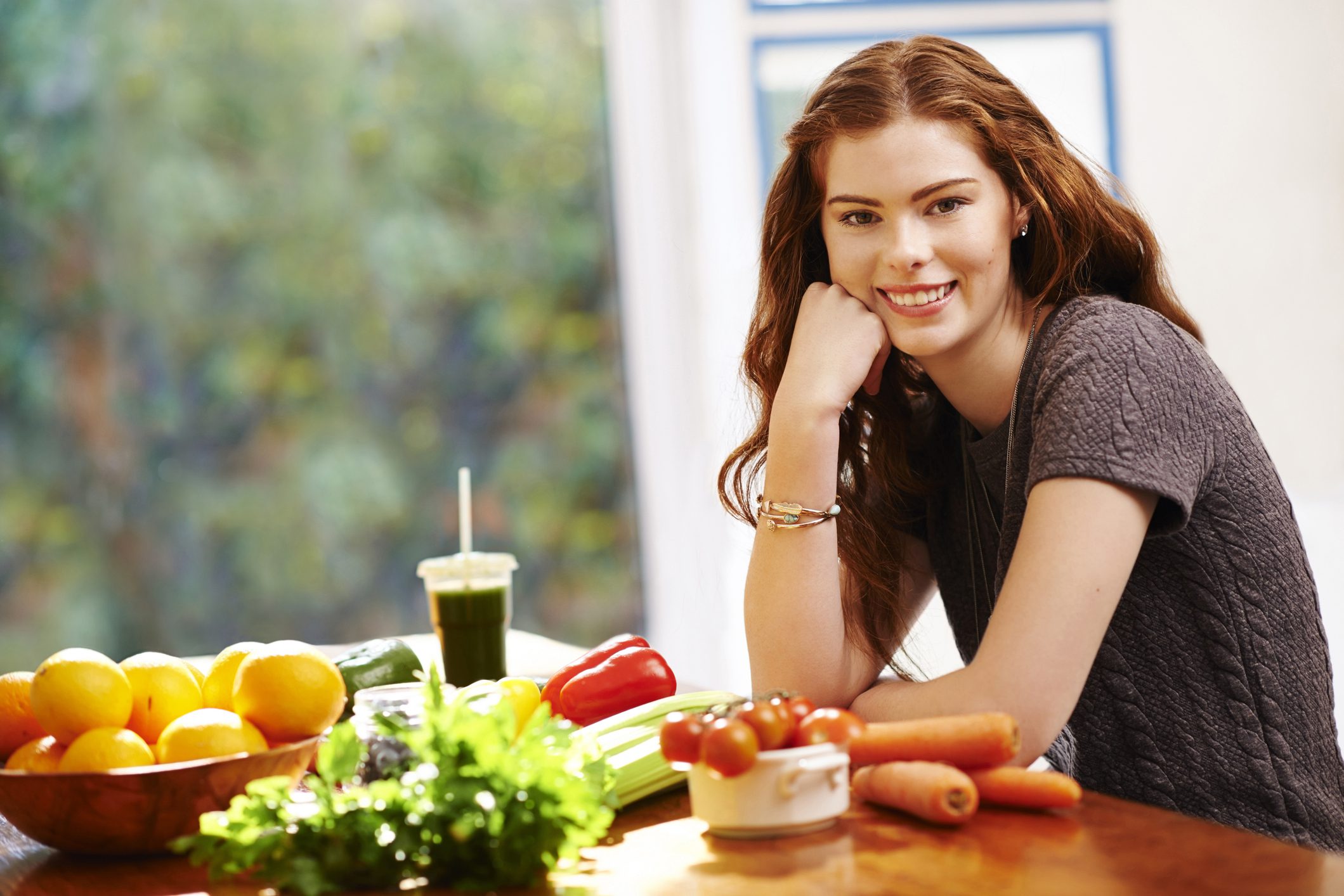 Smiling woman sitting at a table with fresh vegetables and a smoothie.