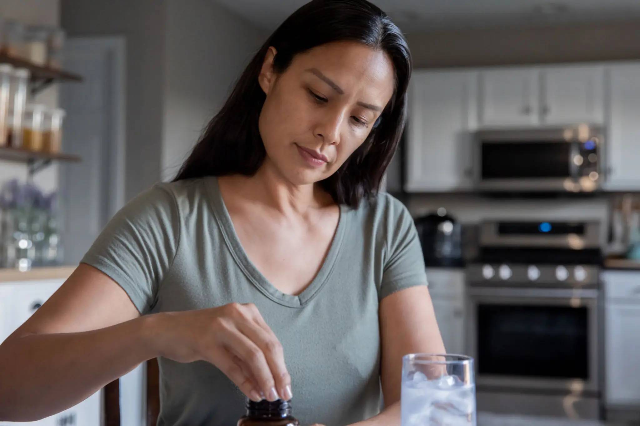 A woman drops liquid from a small bottle into a glass of water.