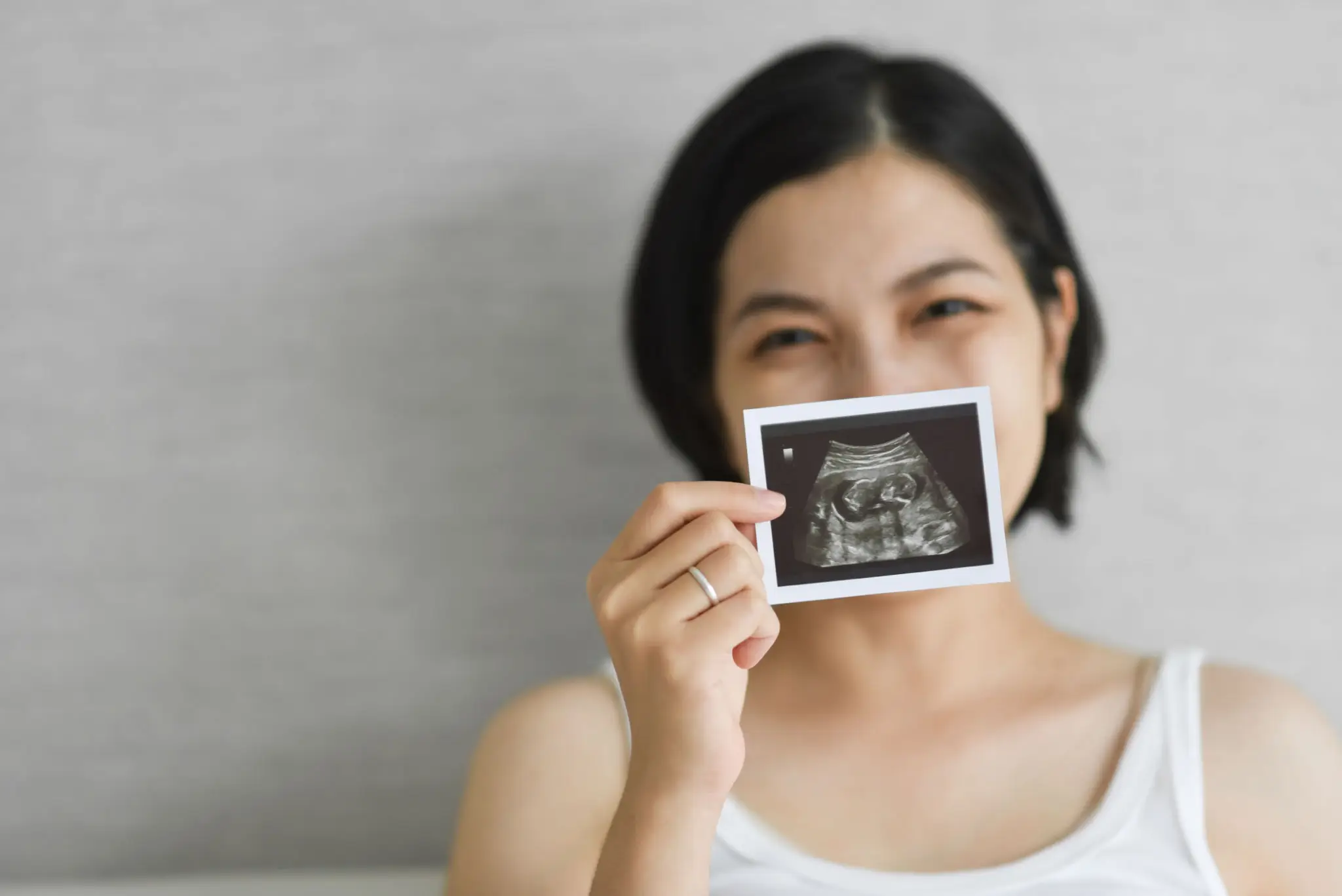 Woman happily holding an ultrasound photo, smiling at the camera.