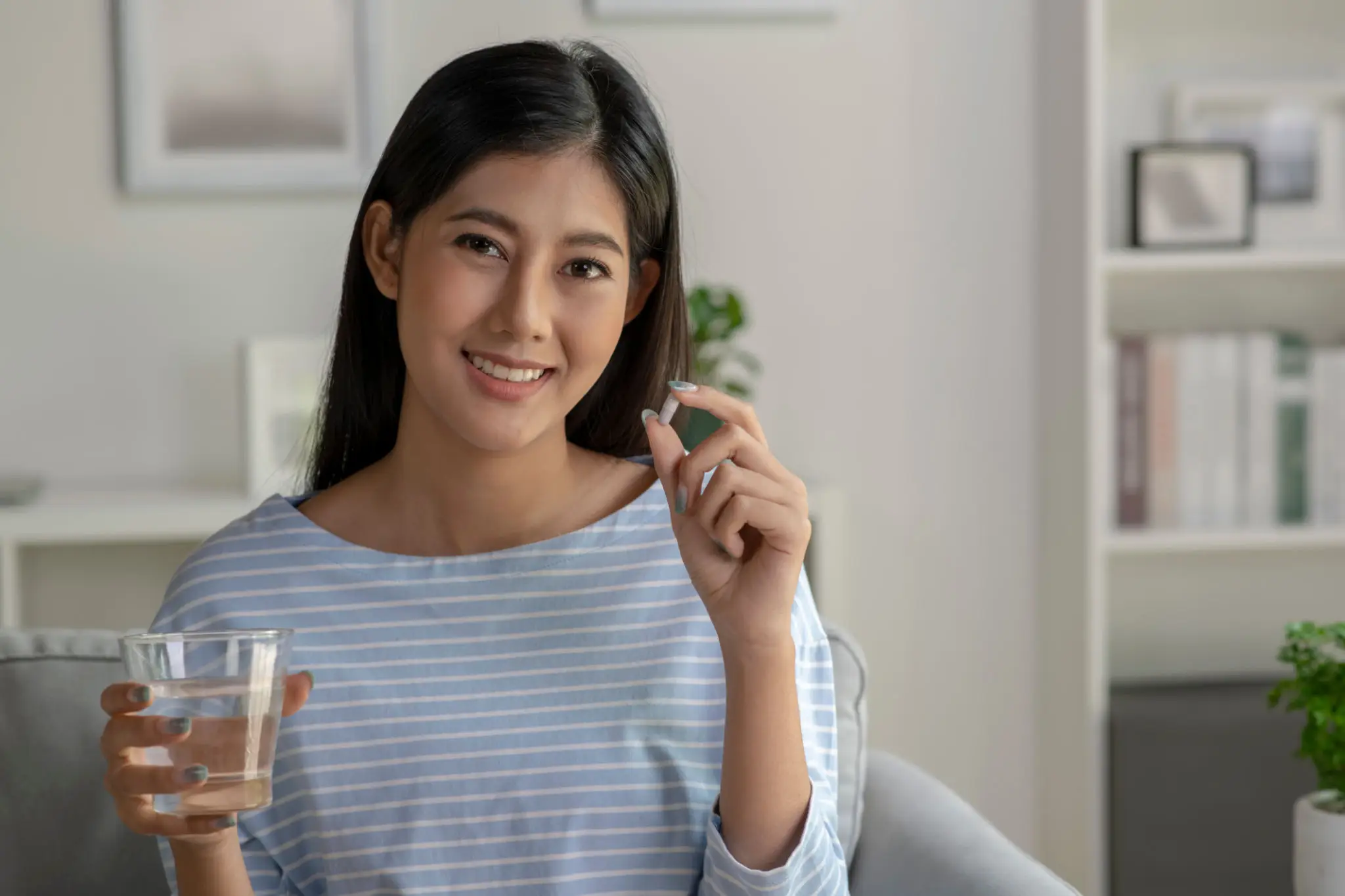 Young woman smiling while holding a pill and water glass.
